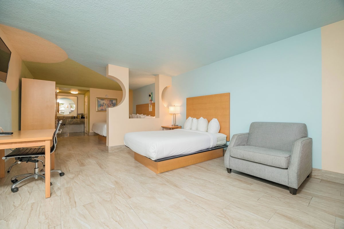A hotel room with a bed, a desk, a chair, and a lamp.