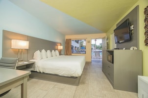 Quarto de hotel com cama, escrivaninha, cadeira, televisão e vista para o exterior.