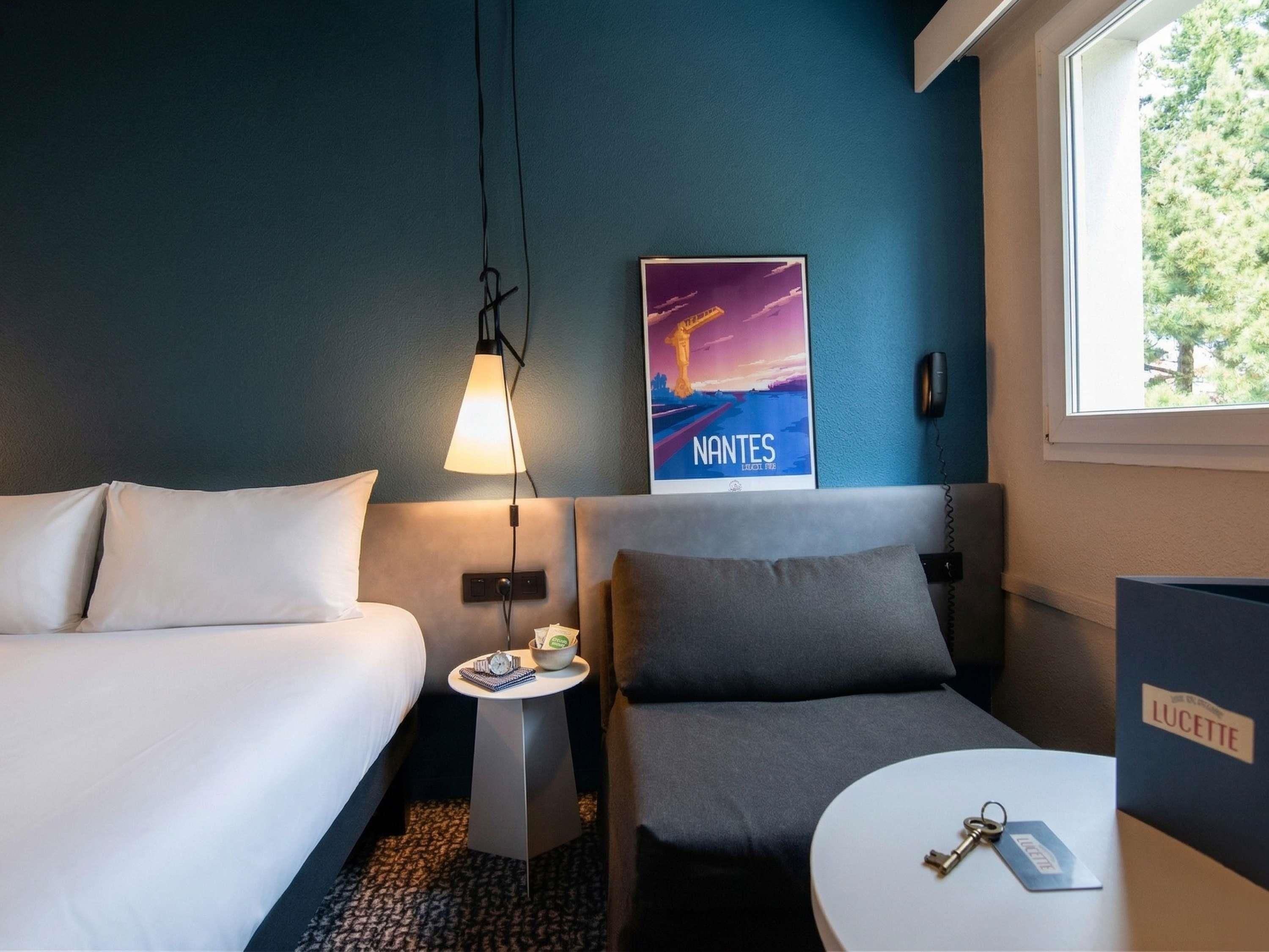 Ein Hotelzimmer mit Bett, Schreibtisch, Stuhl, Lampe, einem Poster und einem Fenster.