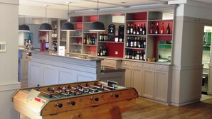 A modern kitchen with a foosball table, a bar area with wine bottles, and a red dining table. - ibis Nantes La Beaujoire Parc Expo (Nantes)