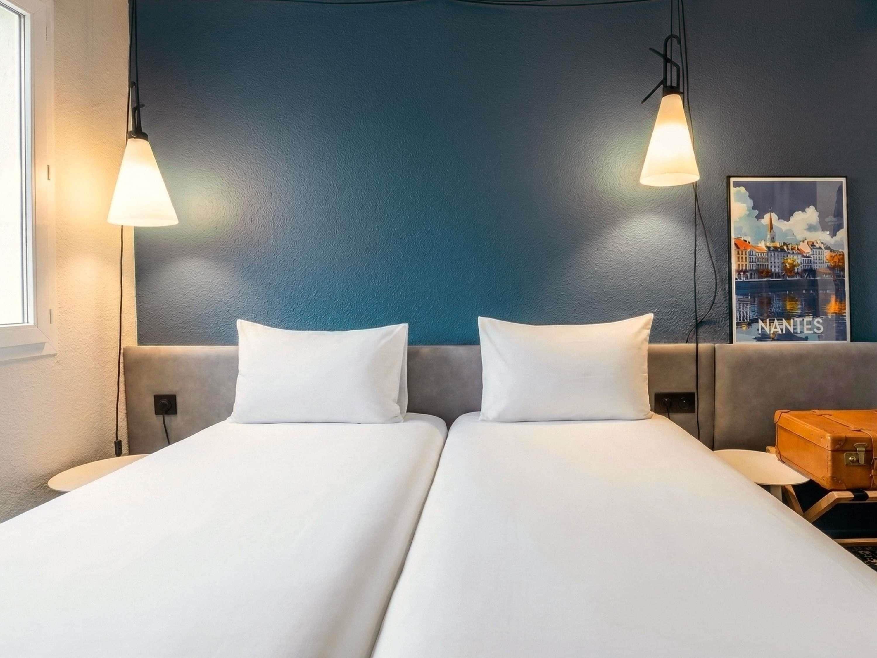 A double bed with white linens, two bedside lamps, a nightstand with a lamp, and a poster on the wall.