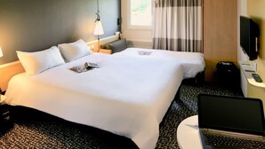 Une chambre d’hôtel avec deux lits, un bureau avec un ordinateur portable, une télévision et une fenêtre avec des rideaux.
