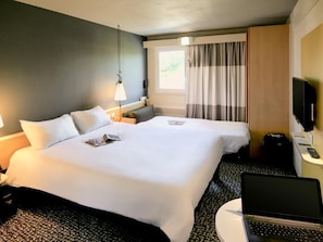 A hotel room with two beds, a desk with a laptop, a TV, and a window with curtains. - ibis Nantes La Beaujoire Parc Expo (Nantes)