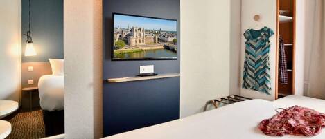 Habitación de hotel con cama, televisor montado en la pared, espejo, mesita de noche y armario.