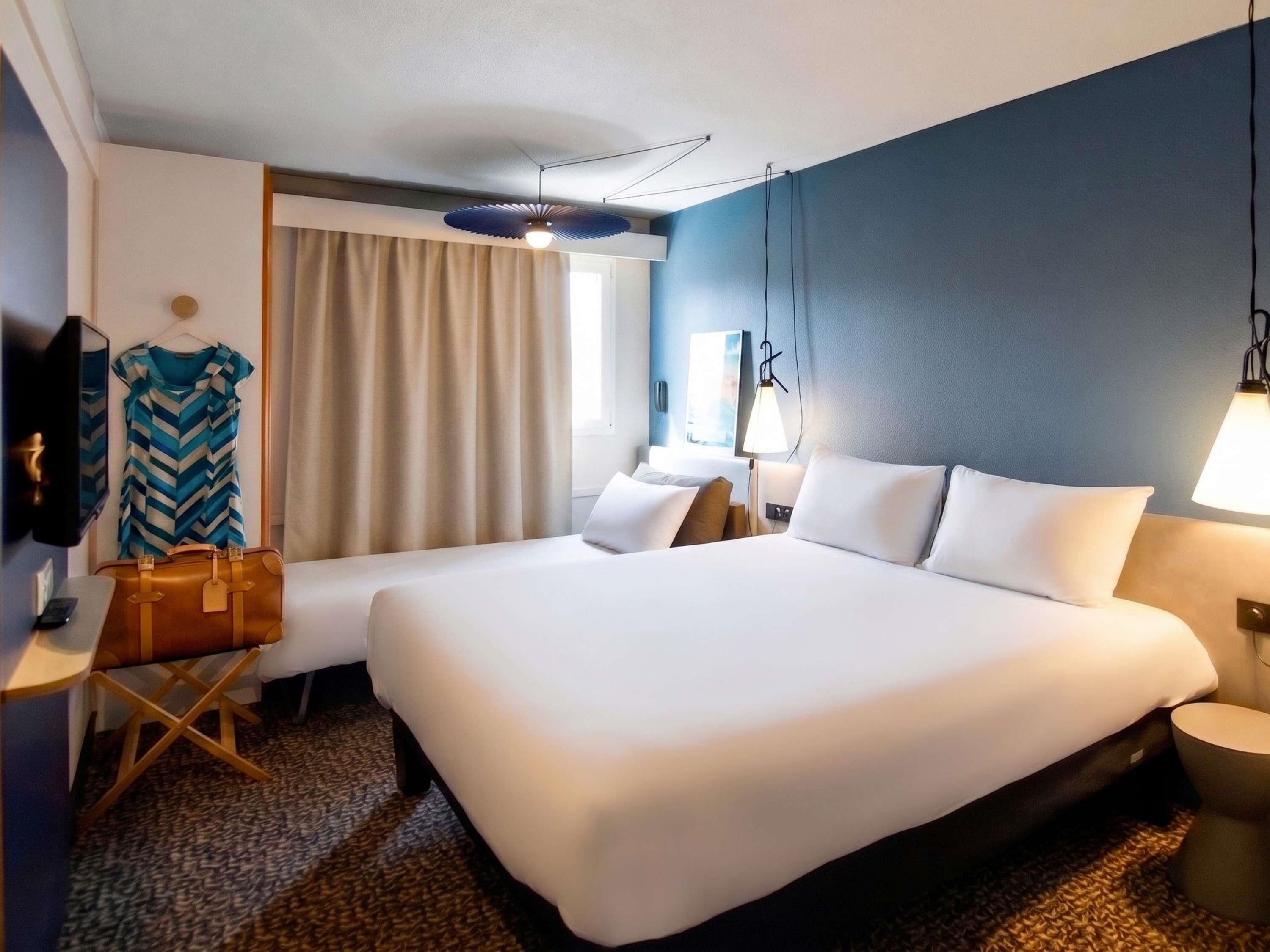 A hotel room with a large bed, a desk, a chair, a television, and a window with curtains.
