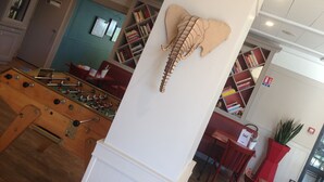A room with a foosball table, a bookshelf, and a large decorative piece resembling a skeleton. - ibis Nantes La Beaujoire Parc Expo (Nantes)