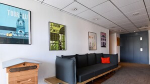 Un hall d’hôtel moderne avec un canapé gris foncé, une table d’appoint en bois et une commode en bois.