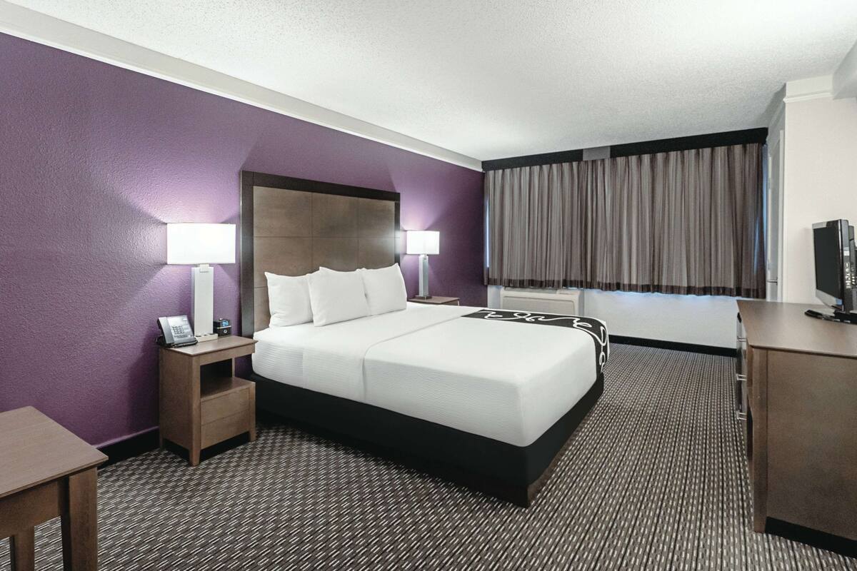 A hotel room with a large bed, a nightstand with a lamp, a desk, and a television.
