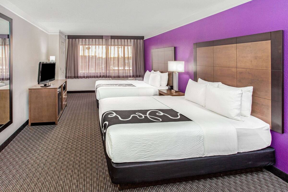 A hotel room with a large bed, a TV, a desk, and a window with curtains.