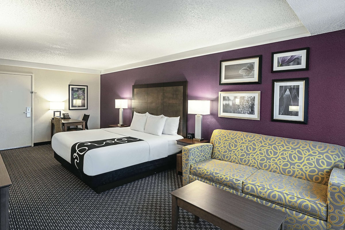A hotel room with a bed, a sofa, a desk, and a chair. There are framed pictures on the wall.