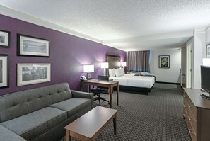 Ein Hotelzimmer mit grauem Sofa, einem Holztisch, einem Bett mit weißer Bettwäsche und einem Fernseher.
