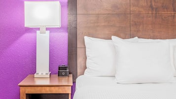 A neatly made bed with white bedding, a bedside table with a lamp, and a wall with a purple texture.