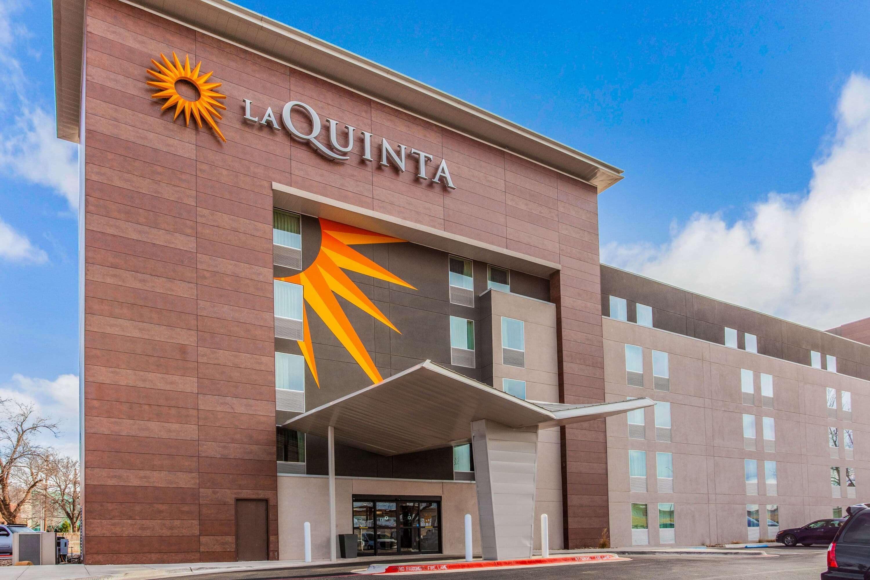 Een La Quinta hotel met een opvallend zonlogo, een overdekte ingang en een parkeerplaats.