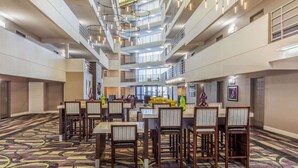 Eine geräumige Hotelhalle mit hoher Decke, mehreren Etagen und einer zentralen Sitzgruppe mit Tischen und Stühlen.