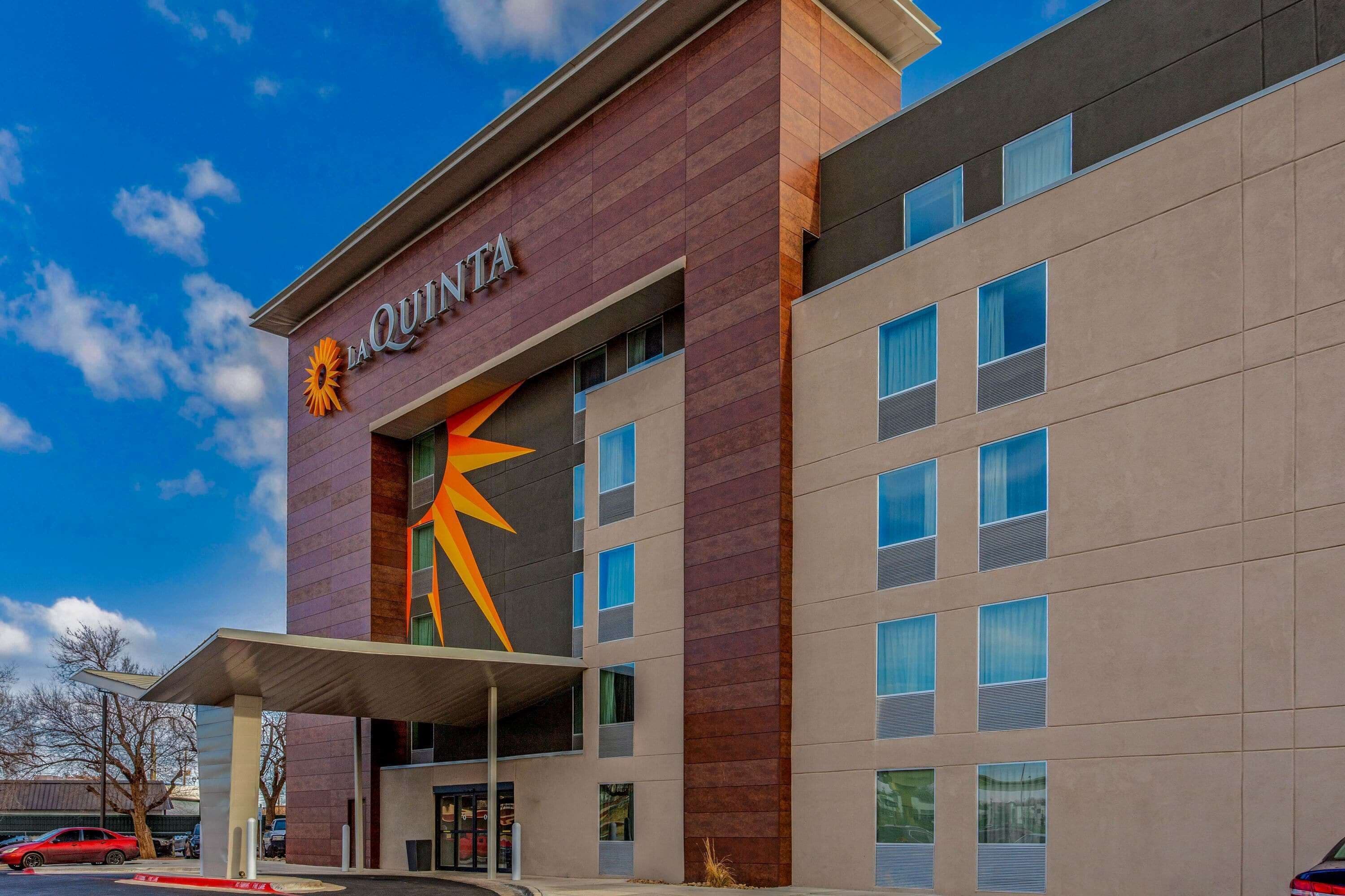 Un hotel moderno con un llamativo letrero de 'La Quinta', múltiples ventanales y un área de entrada techada.