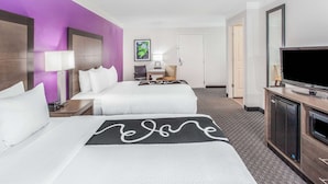 Ein Hotelzimmer mit zwei Betten, einem Schreibtisch, einem Stuhl, einem Fernseher und einer Mikrowelle.