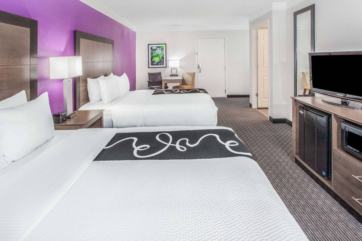 A hotel room with two beds, a desk, a chair, a television, and a microwave.