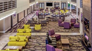 Eine geräumige Hotelhalle mit mehreren Sitzbereichen, darunter gelbe und violette Sofas sowie verschiedene Tische und Stühle.