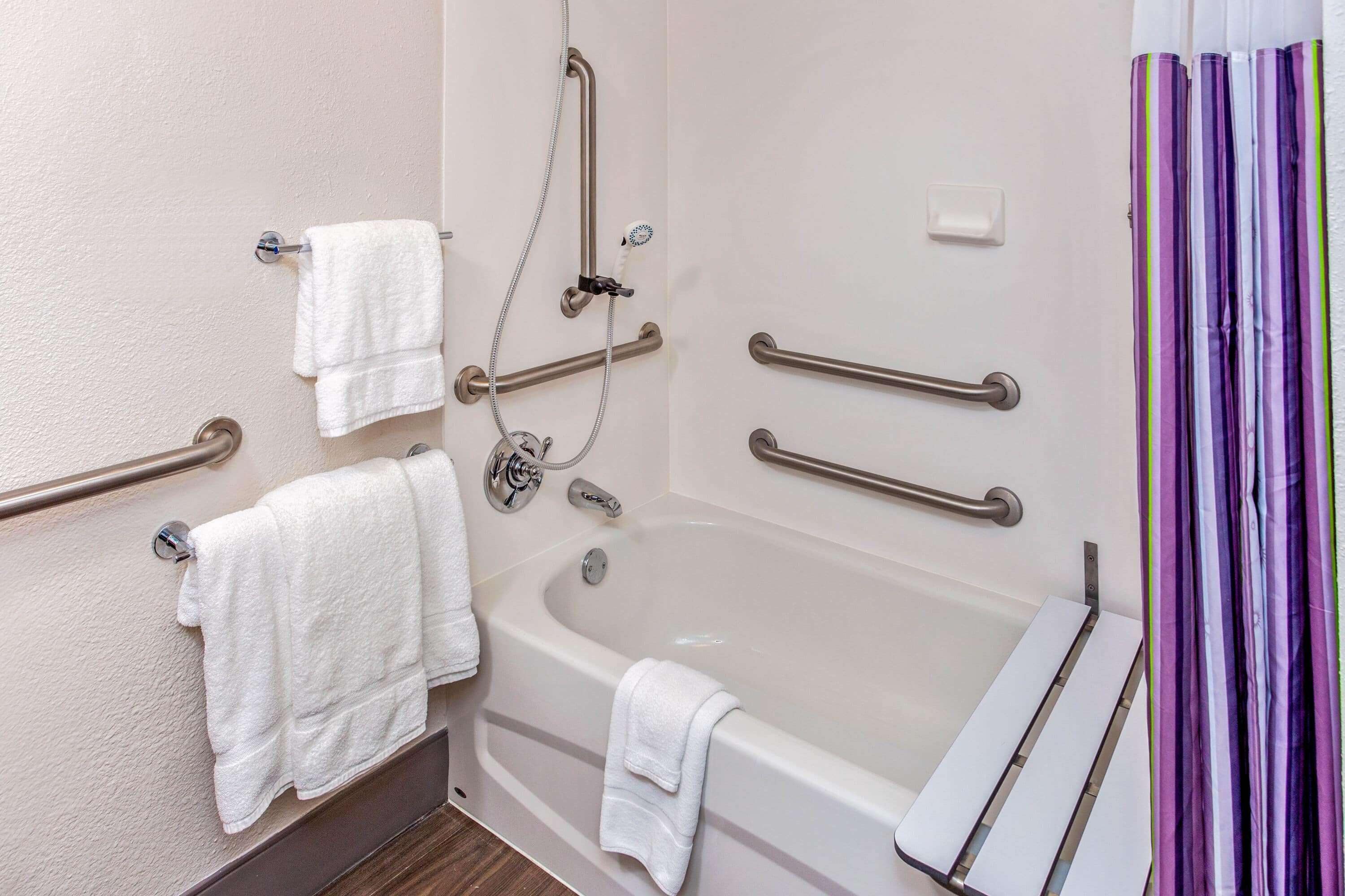 A bathroom with a bathtub, grab bars, and a shower control panel.