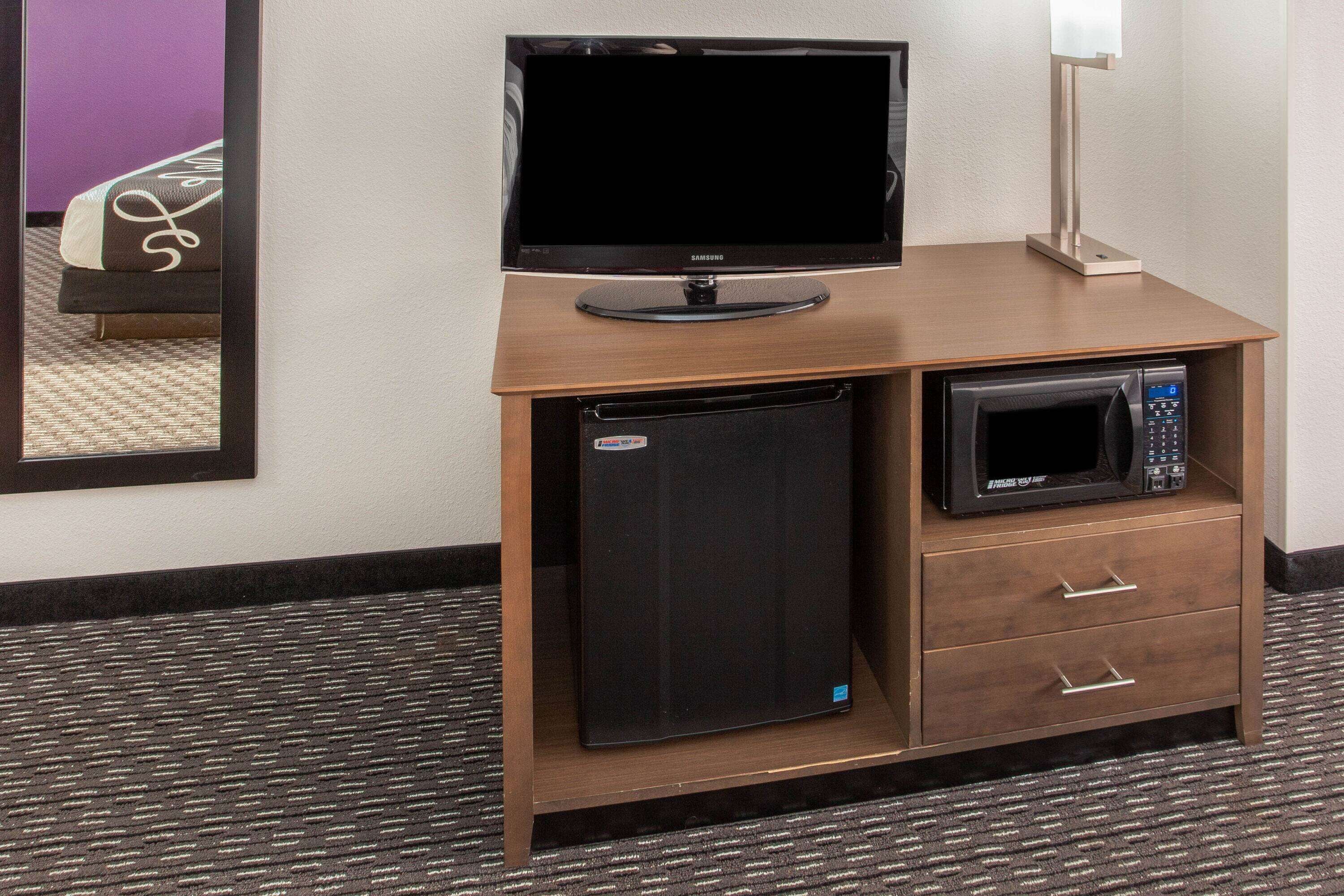 A hotel room with a wooden desk, a flat-screen TV, a microwave, and a refrigerator.