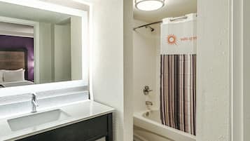 A bathroom with a white sink, a mirror, a shower with a striped curtain, and a ceiling light.