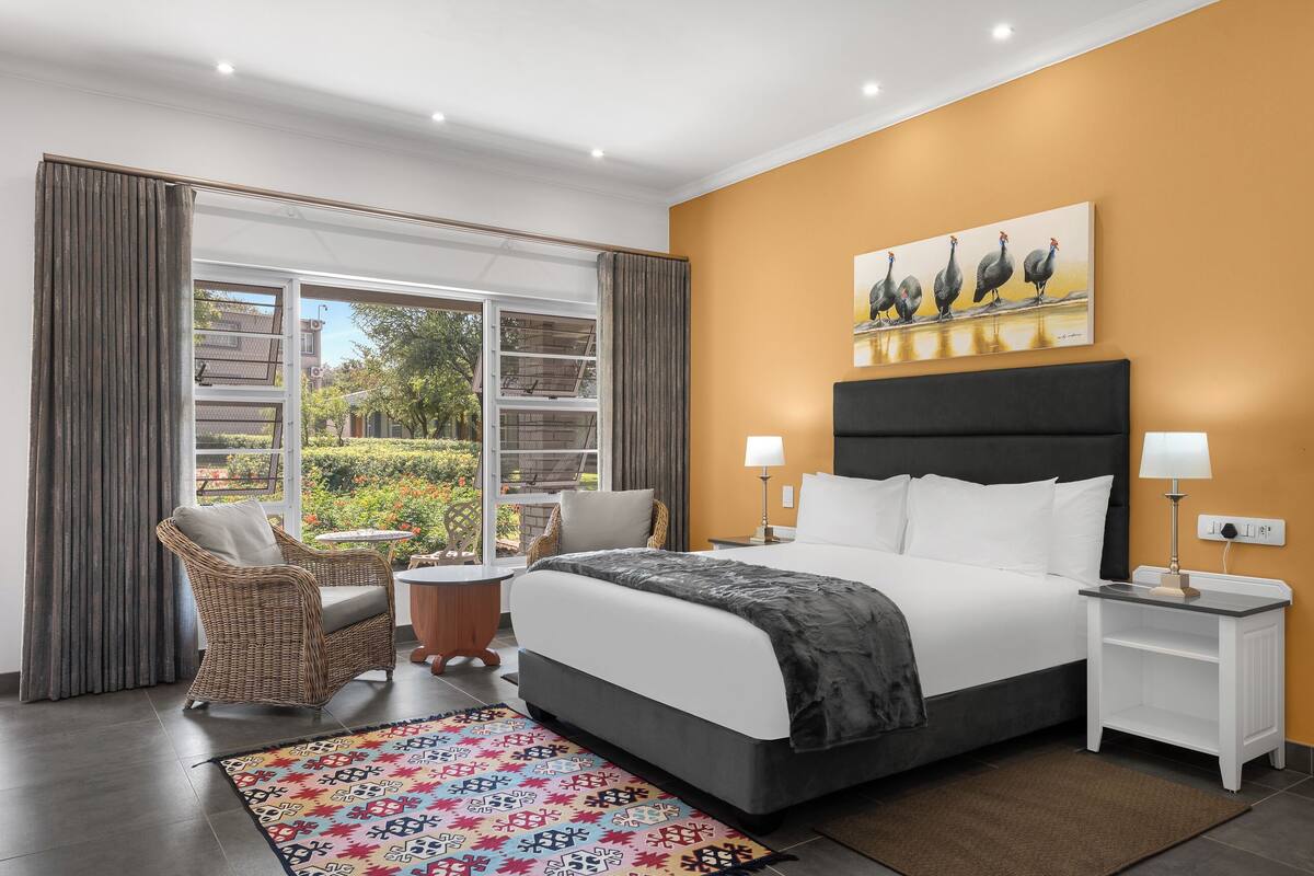 Une chambre d’hôtel moderne dotée d’un grand lit, d’un coin salon avec un fauteuil et une petite table, et offrant une vue sur l’extérieur.