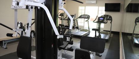 Ein Fitnessstudio mit verschiedenen Trainingsgeräten, darunter Laufbänder, ein Kraftgerät und Bänke.