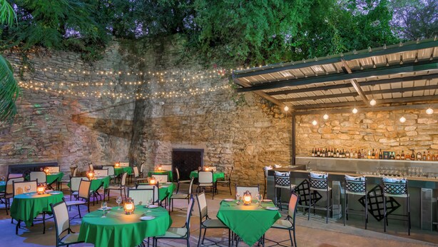 An outdoor dining area with stone walls, string lights, and a bar with bottles. Tables are set with chairs and candles. - Park Hotel Mokopane (Mogalakwena)