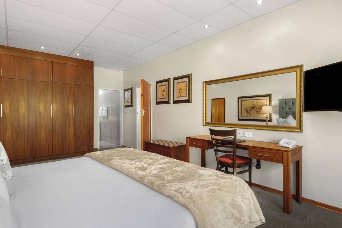 Une chambre d’hôtel comprenant un lit, une armoire en bois, un bureau, une chaise et un téléviseur.