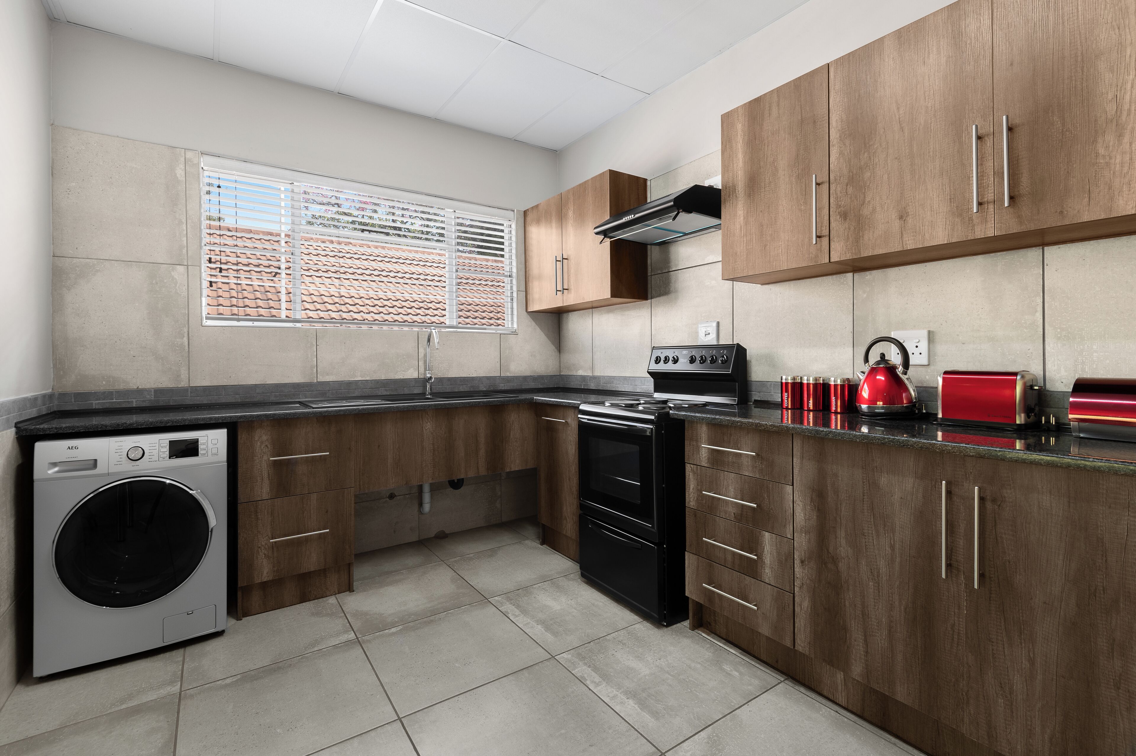 A kitchen with wooden cabinets, a washing machine, a stove, and a red kettle.