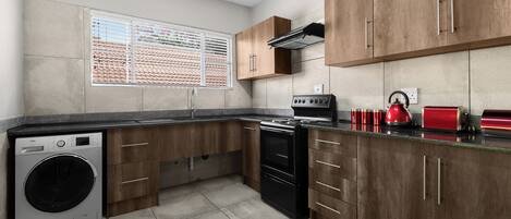 A kitchen with wooden cabinets, a washing machine, a stove, and a red kettle.