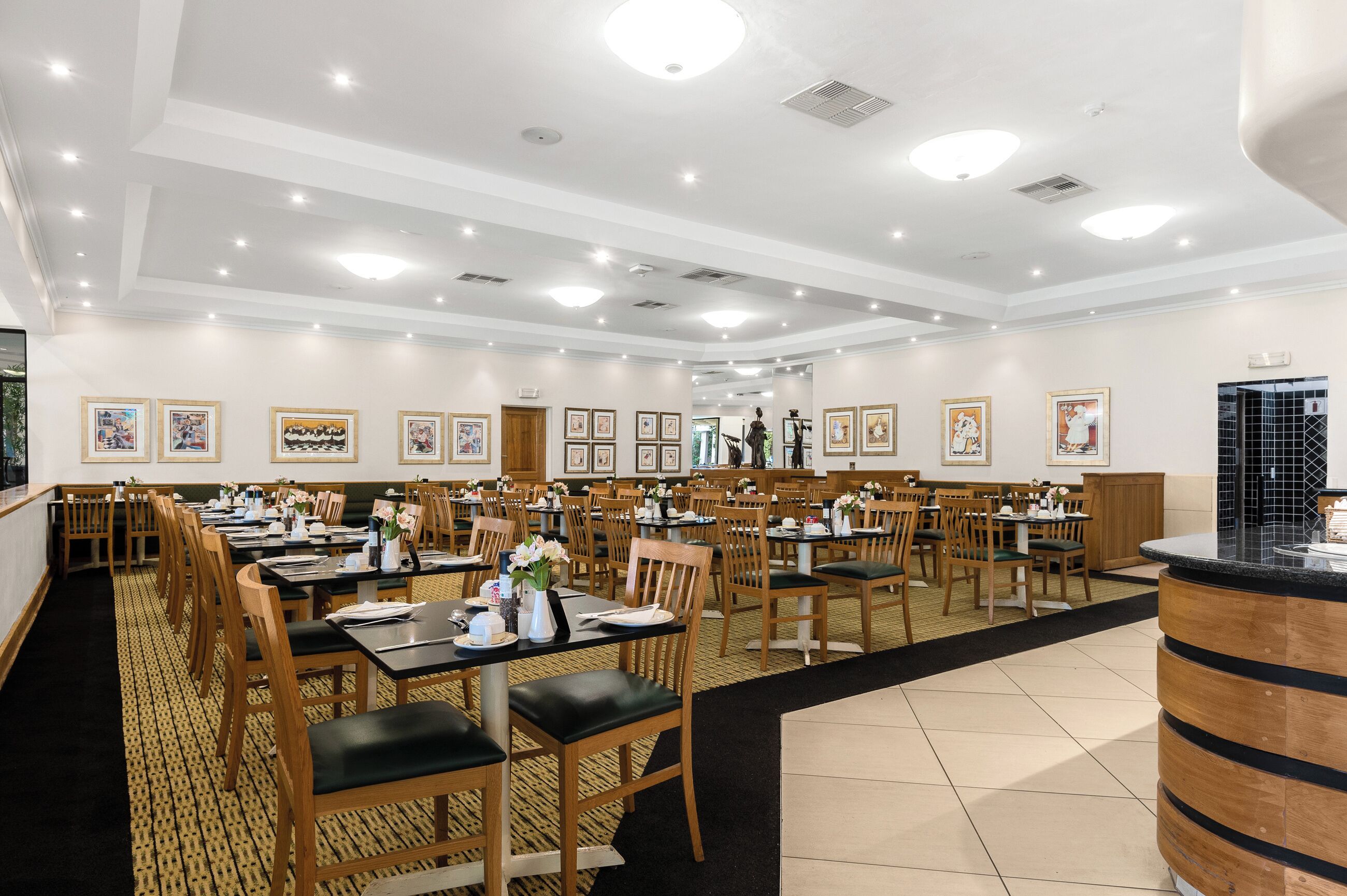 Un comedor amplio con varias mesas y sillas, una barra central y cuadros en las paredes.