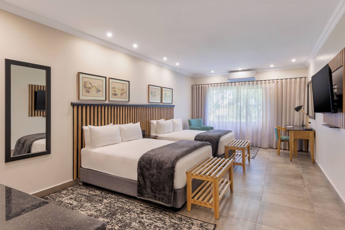 Une chambre d’hôtel avec deux lits, un bureau, une chaise, un téléviseur et des œuvres d’art encadrées au mur.