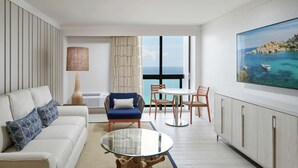 A modern living room with a glass coffee table, a sofa with patterned cushions, a blue armchair, and a dining area with a view of the sea. - Bahia Mar Ft. Lauderdale Beach- a DoubleTree by Hilton Hotel (Fort Lauderdale)
