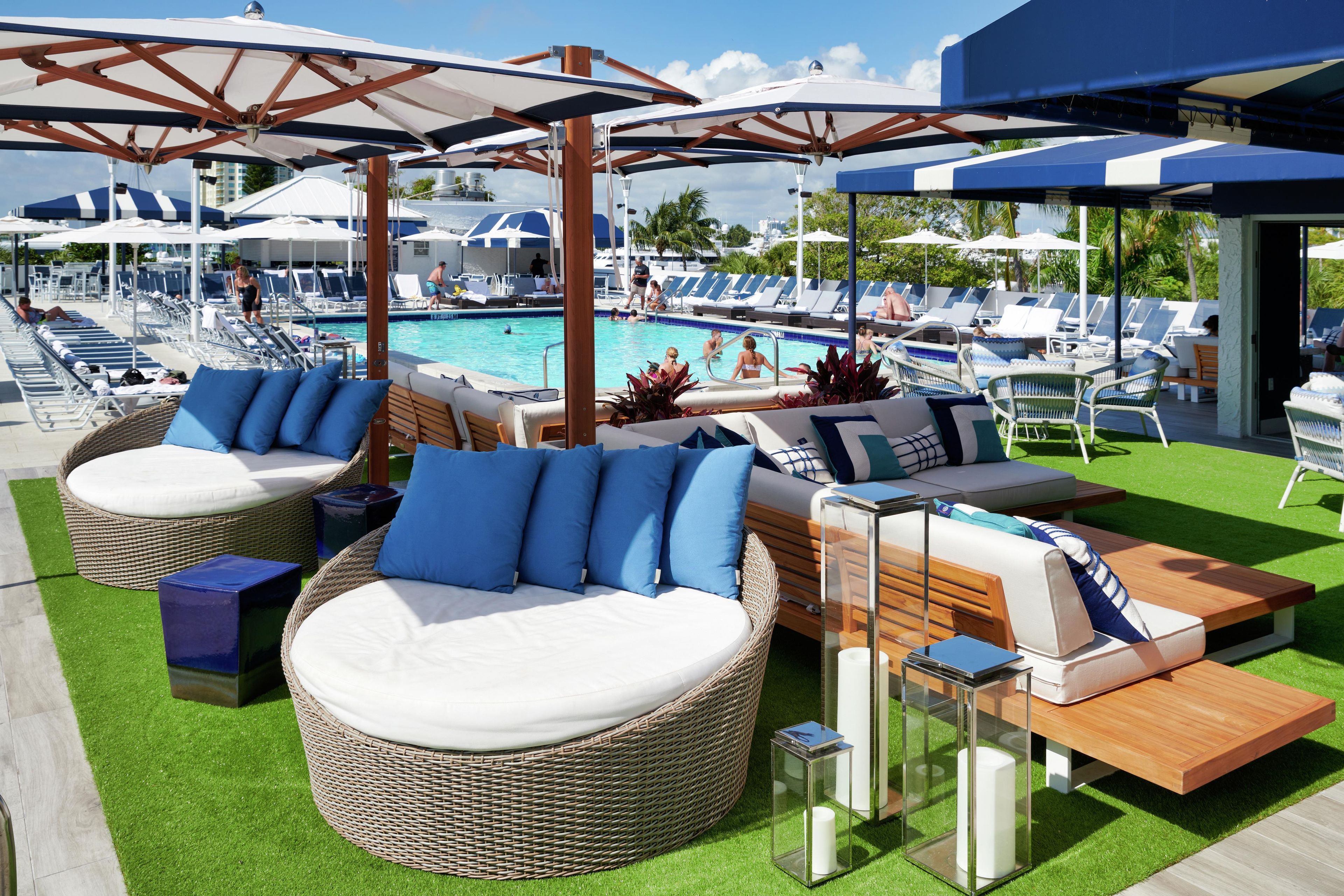 Zona junto a la piscina con mobiliario de mimbre, sombrillas y sillones reclinables.