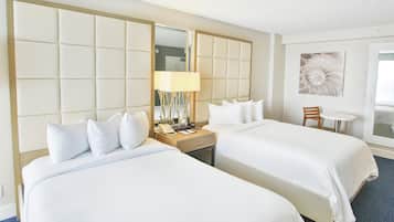 Habitación de hotel con dos camas, una mesita de noche con lámpara, una pequeña mesa con silla y un espejo grande.