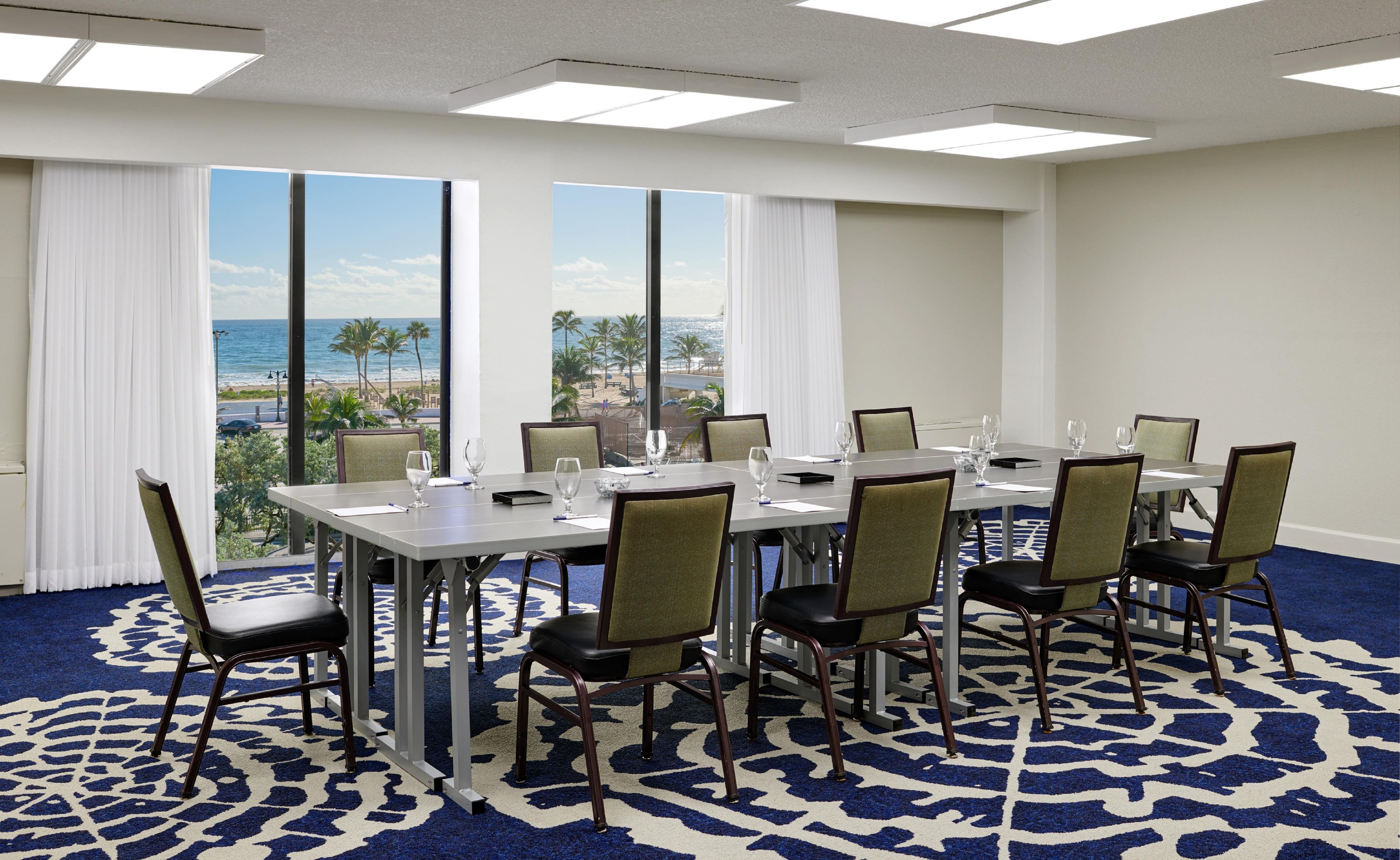 A conference room with a view of the beach, equipped with a table, chairs, and glassware.