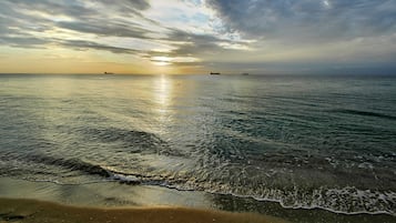 Een strand met kalm water en een zonsondergang.