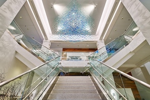Un interior moderno con una escalera central, barandillas de vidrio e instalación decorativa en el techo.