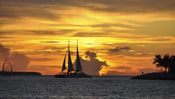 Een zonsondergang boven de oceaan met zeilboten en een eiland in de verte.