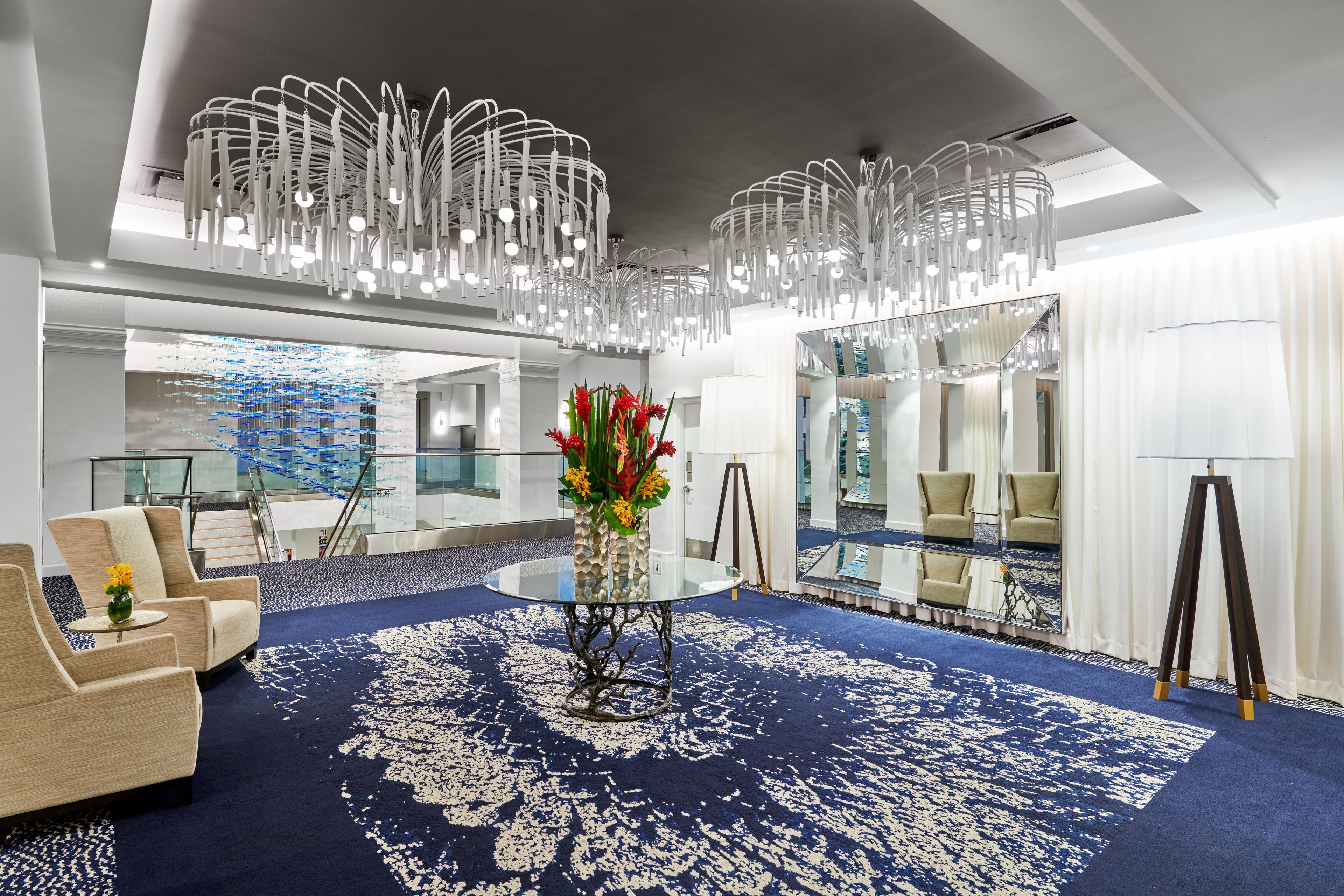 Um hall moderno com carpete azul, área de estar e uma parede de vidro decorativa.