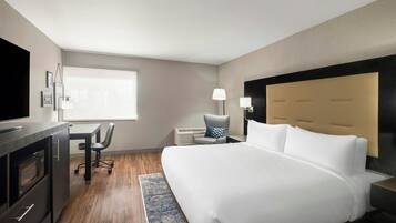 A hotel room with a bed, a desk, a chair, a TV, a lamp, and a window.