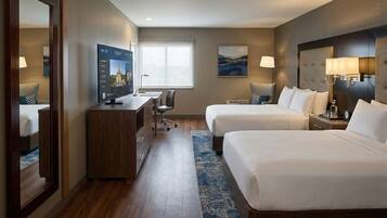 A hotel room with two beds, a desk, a TV, and a large window.