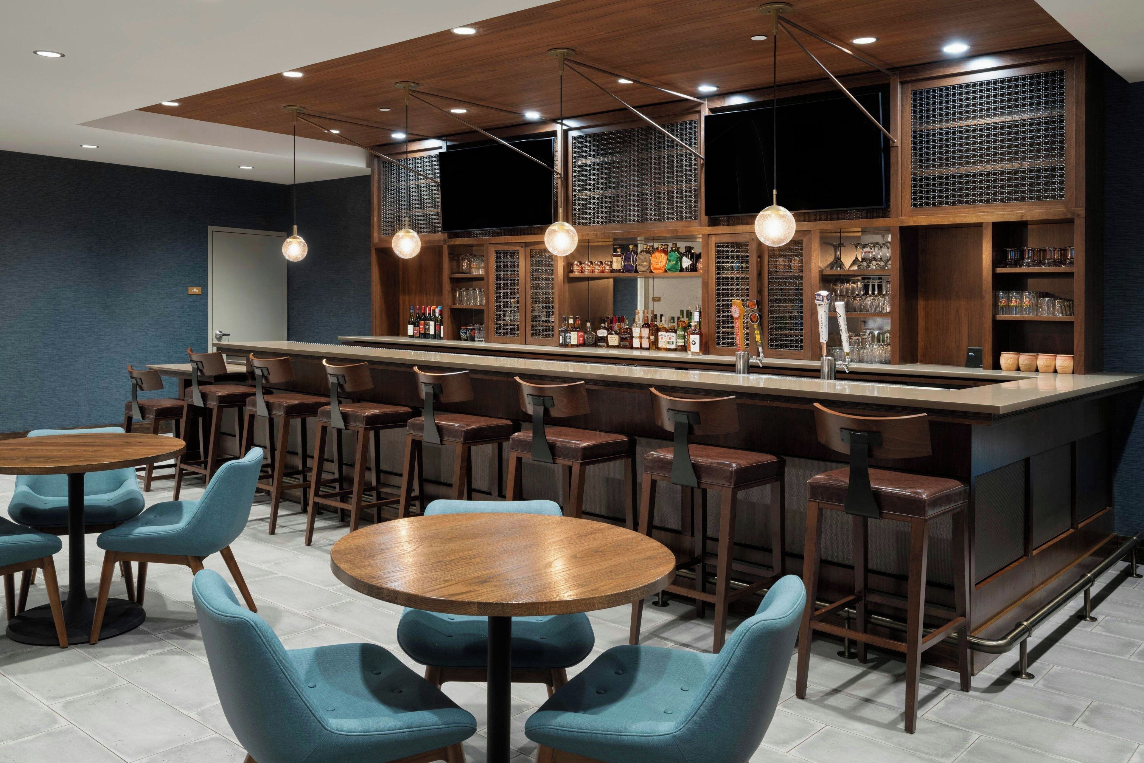 A bar area with a long counter, multiple stools, and a seating area with round tables and chairs.