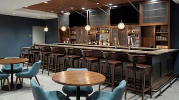 A bar area with a long counter, multiple stools, and a seating area with round tables and chairs.