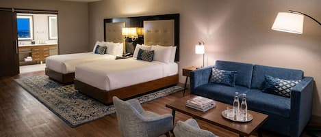 A hotel room with two beds, a sofa, a coffee table, and a desk.