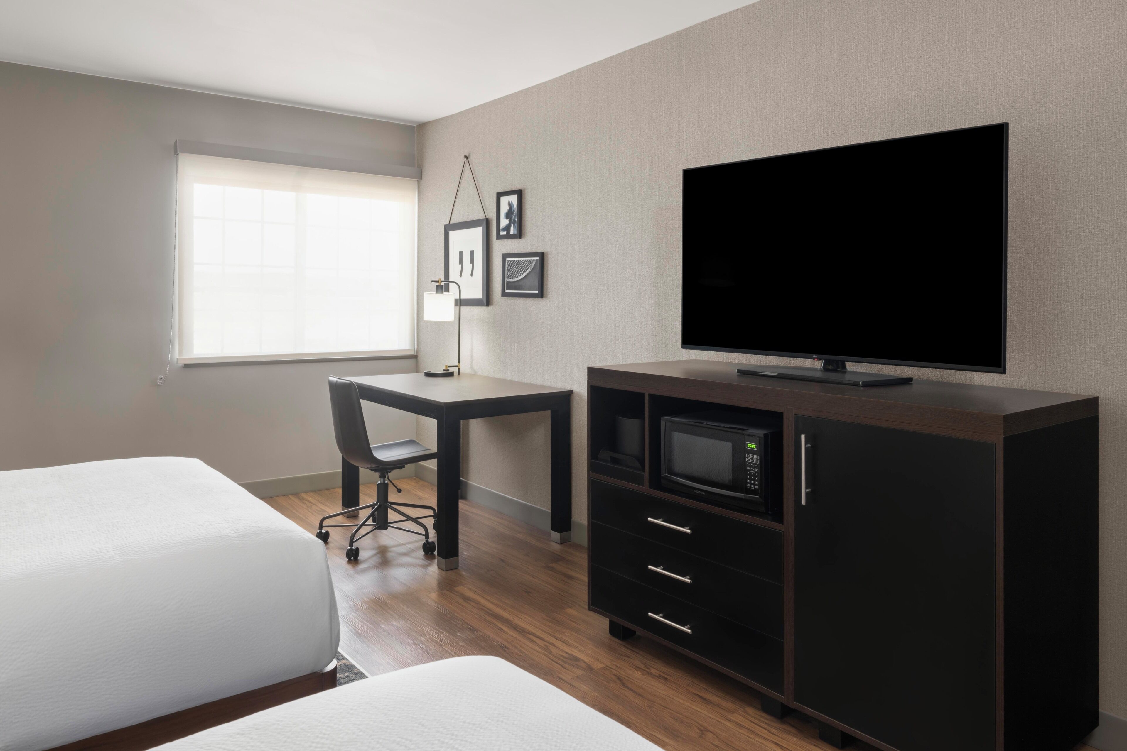Una habitación de hotel con cama, escritorio, televisor, microondas y armario.