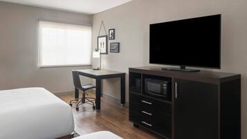 Una habitación de hotel con cama, escritorio, televisor, microondas y armario.