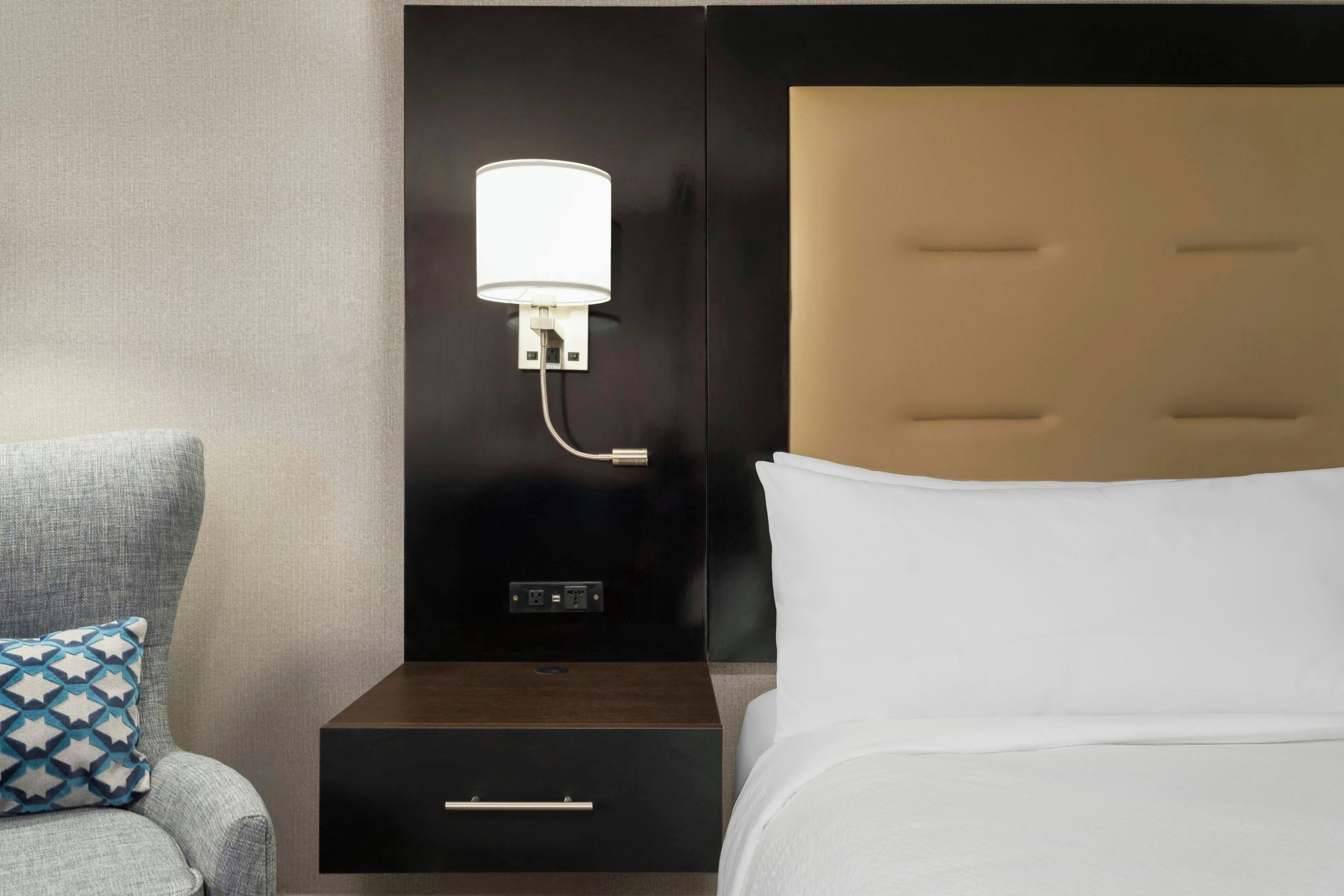 A hotel room with a bed, a nightstand with a lamp, and a drawer unit.