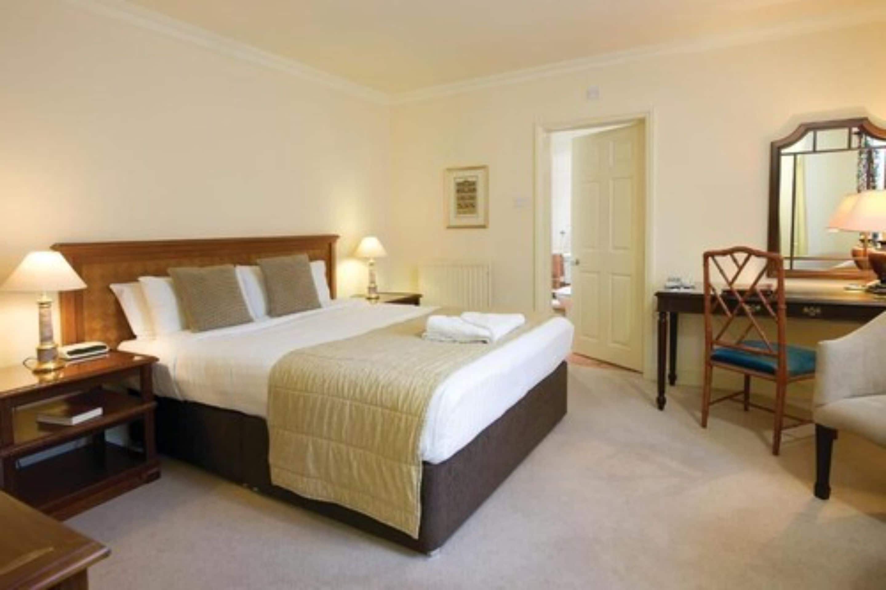 A neatly arranged hotel room with a large bed, bedside tables with lamps, a desk, and a chair.